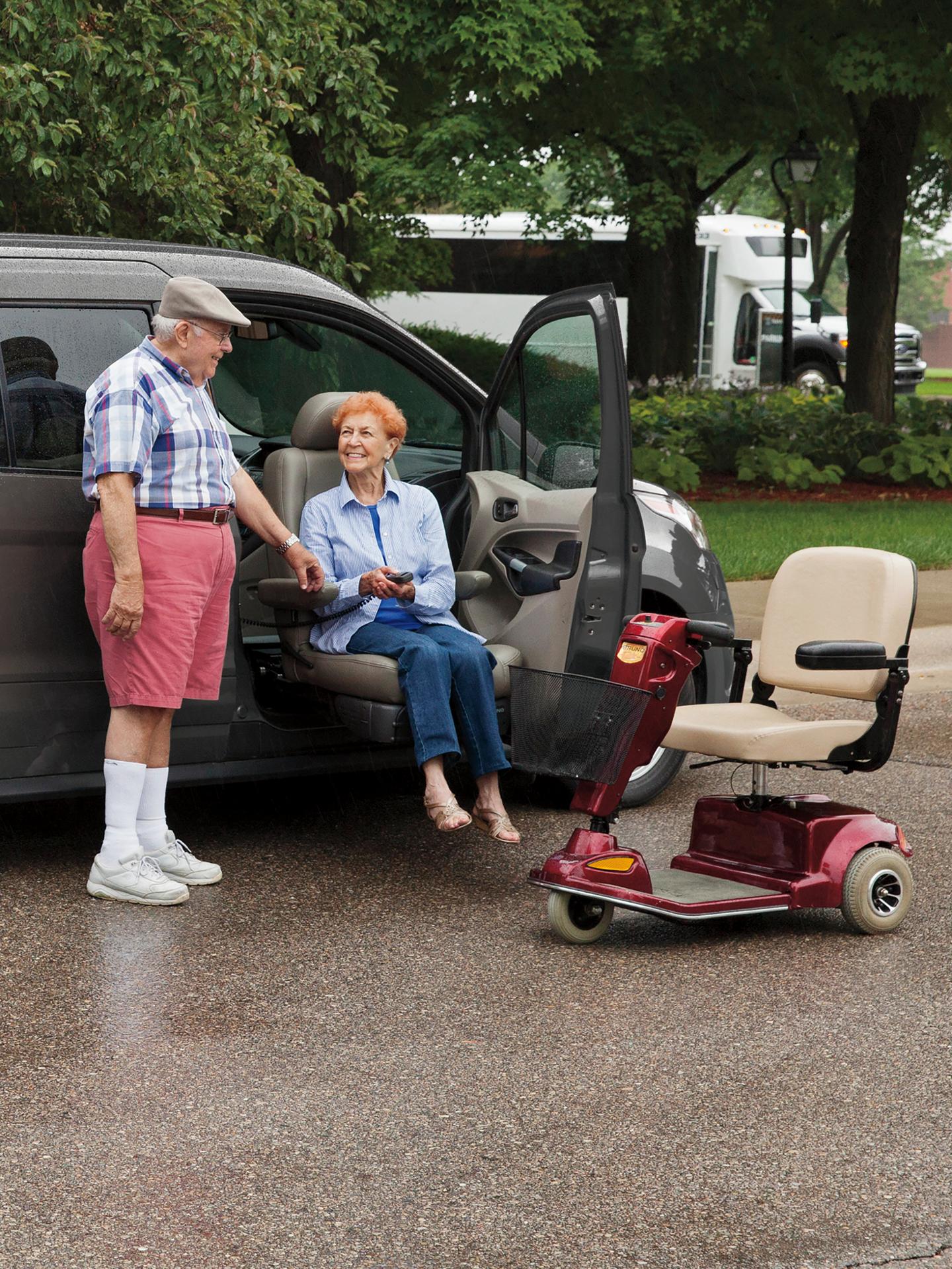 A man helping a woman out of a Ford vehicle, with a mobility scooter nearby