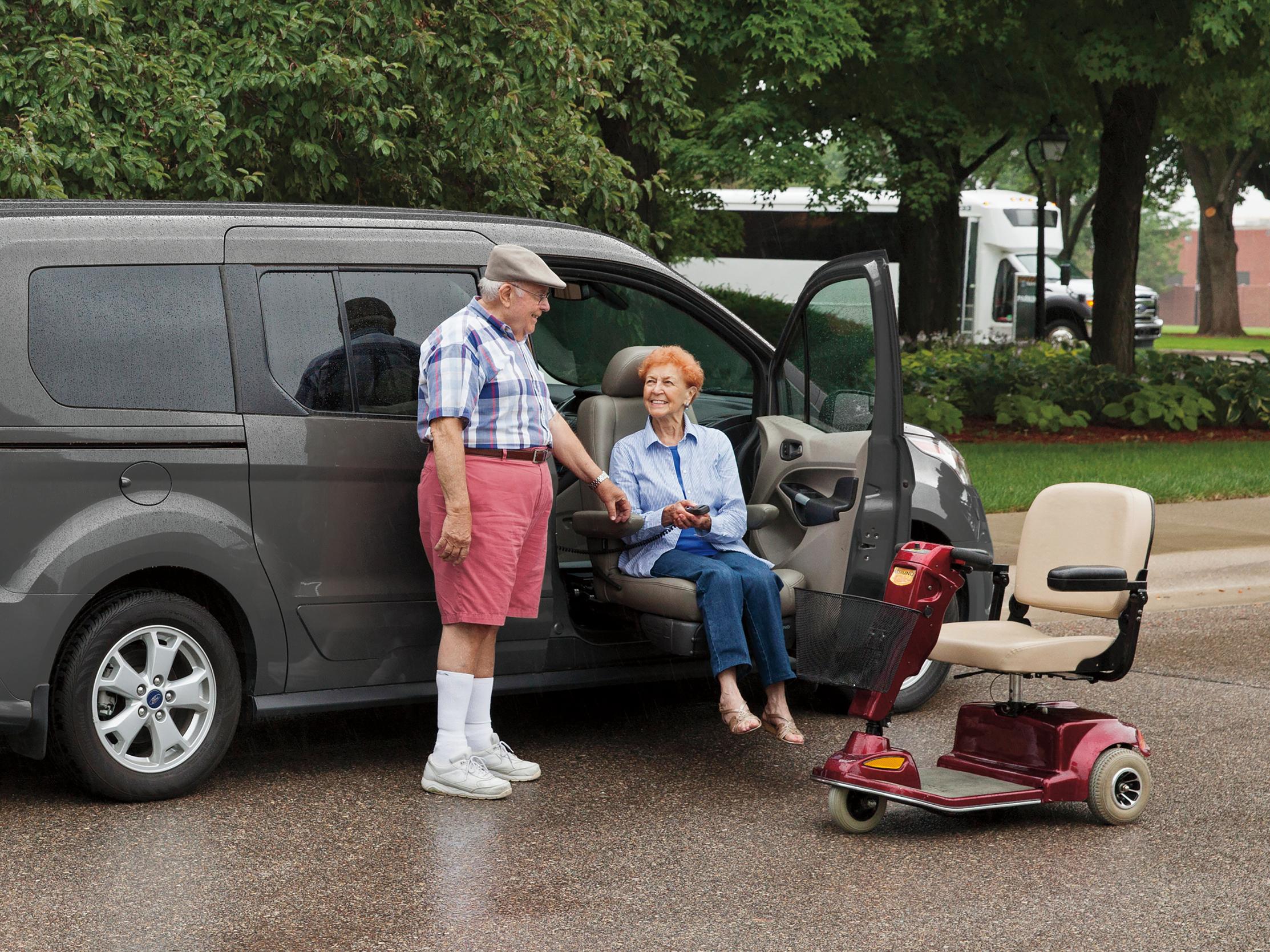 A man helping a woman out of a Ford vehicle, with a mobility scooter nearby
