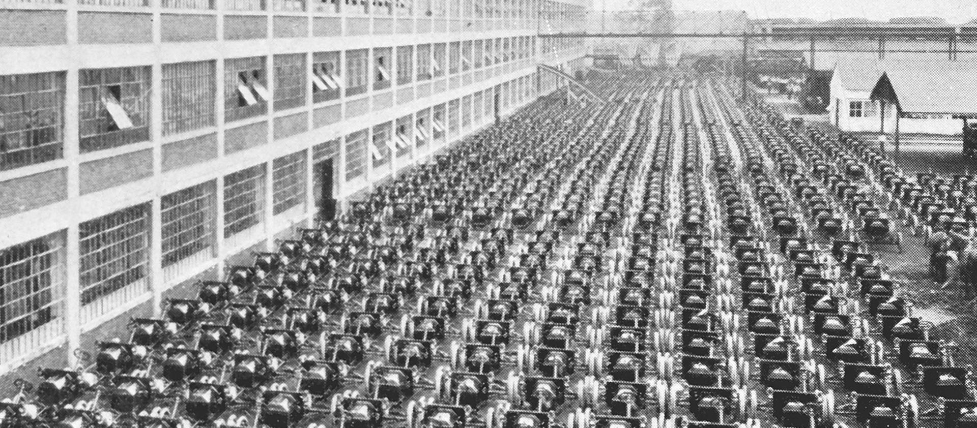A black and white photo of hundreds of automobiles lined up in front of a Ford plant