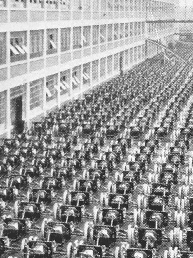 A black and white photo of hundreds of automobiles lined up in front of a Ford plant