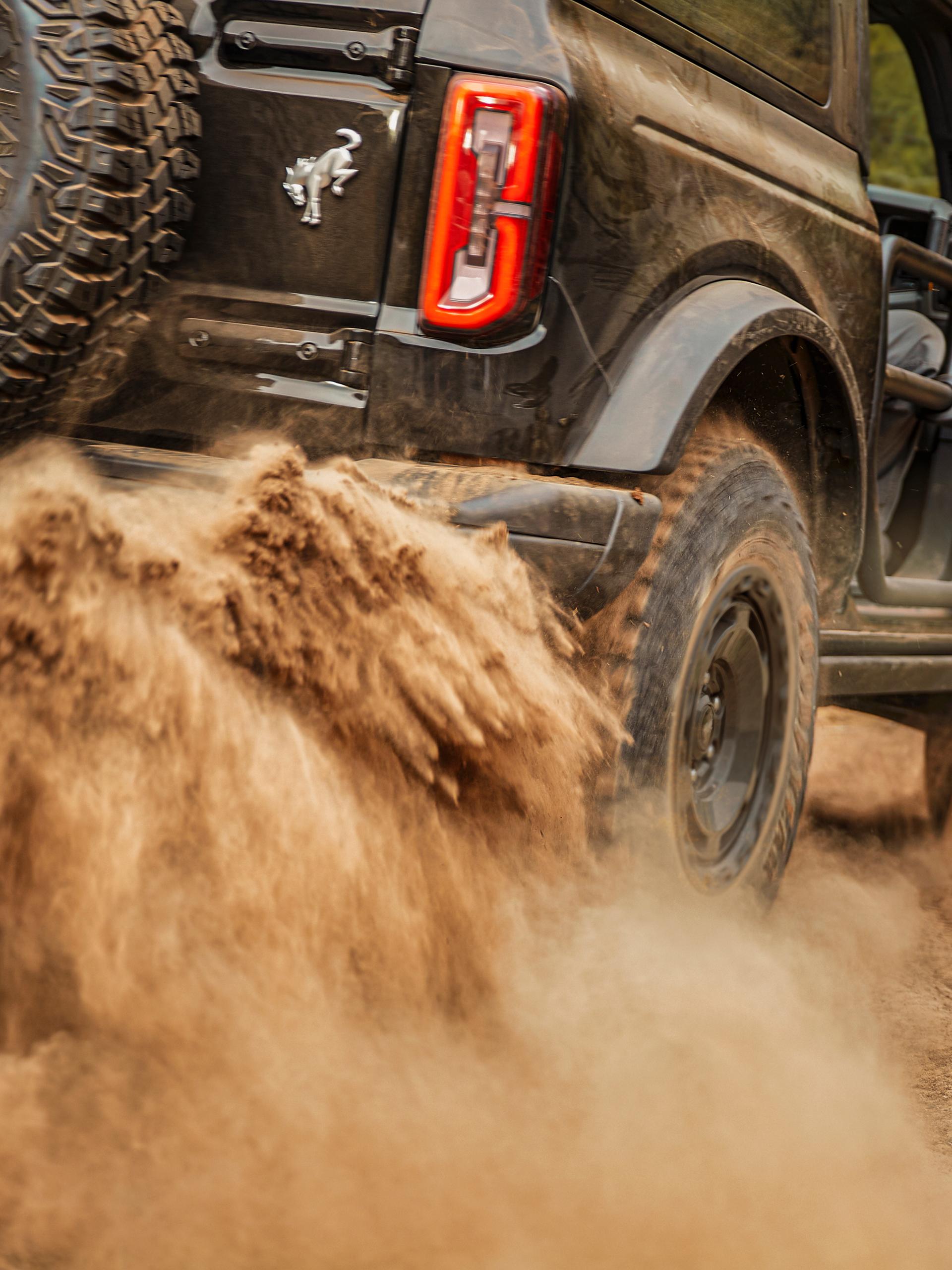 A close-up of the rear tire of a Ford Bronco® SUV kicking up sand and dirt