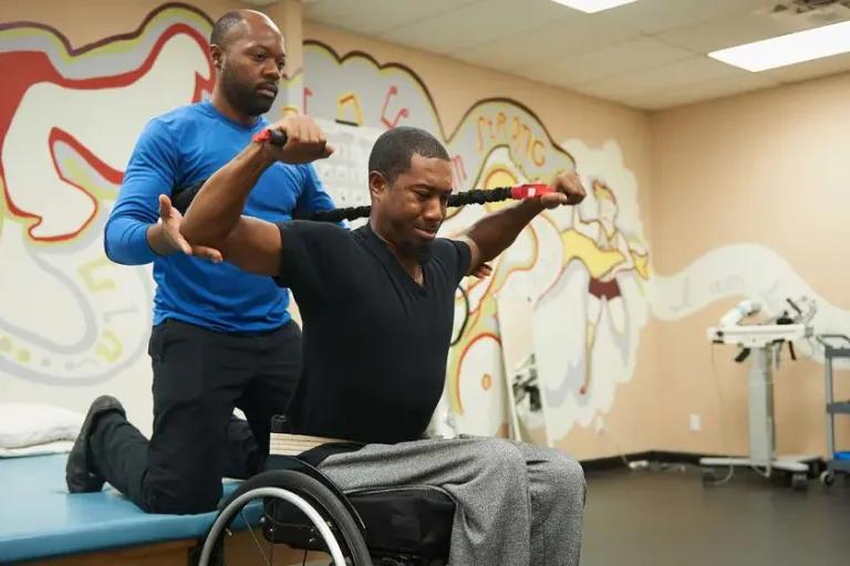 Driver rehabilitation specialist spotting man in a wheelchair using exercise equipment