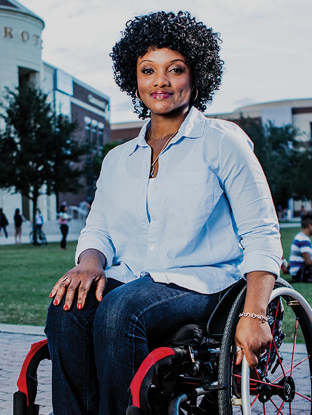 A veteran in a wheelchair smiles, a campus park in the background