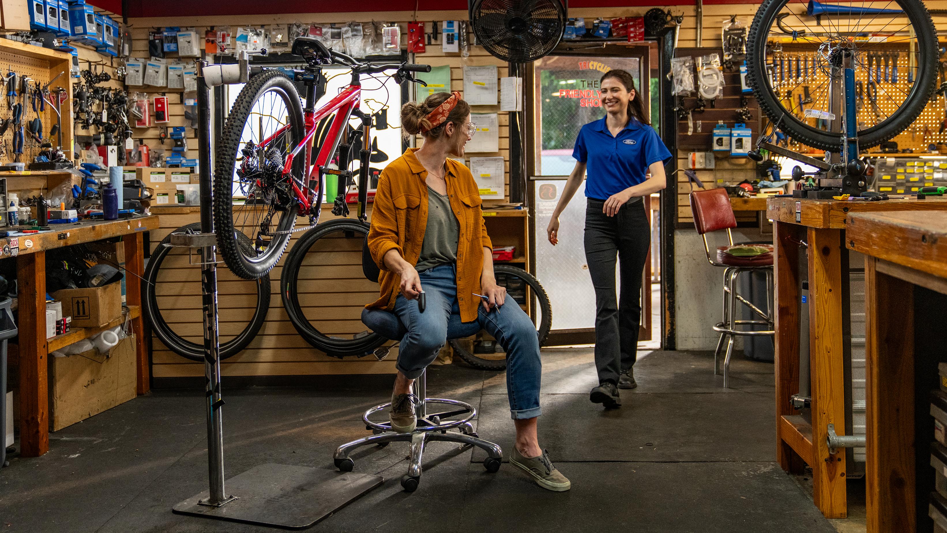 A Ford service tech enters a bicycle shop and picks up keys from an employee