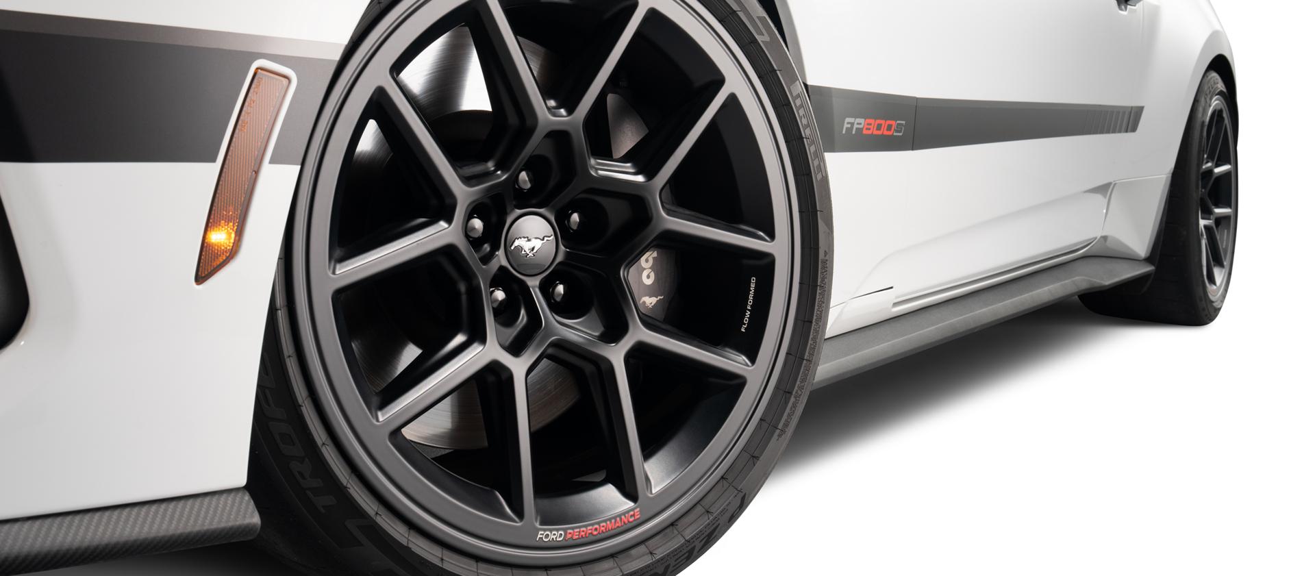 Close-up of the driver-side front black R1 wheel on the white Mustang with side stripe graphics
