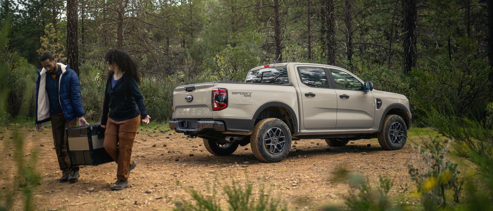 Two people carrying a cooler away from their 2026 Ford Ranger® XLT, which is parked in the woods