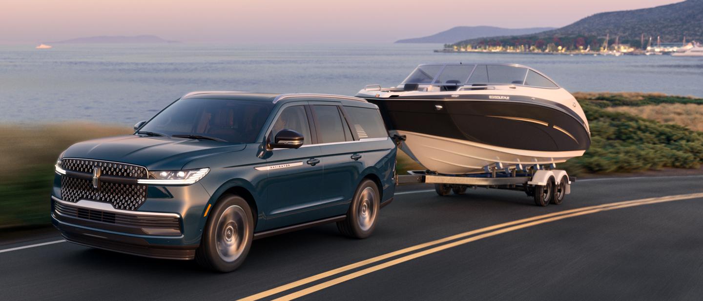 A 2025 Lincoln Navigator® SUV towing a boat is being driven along a curving road