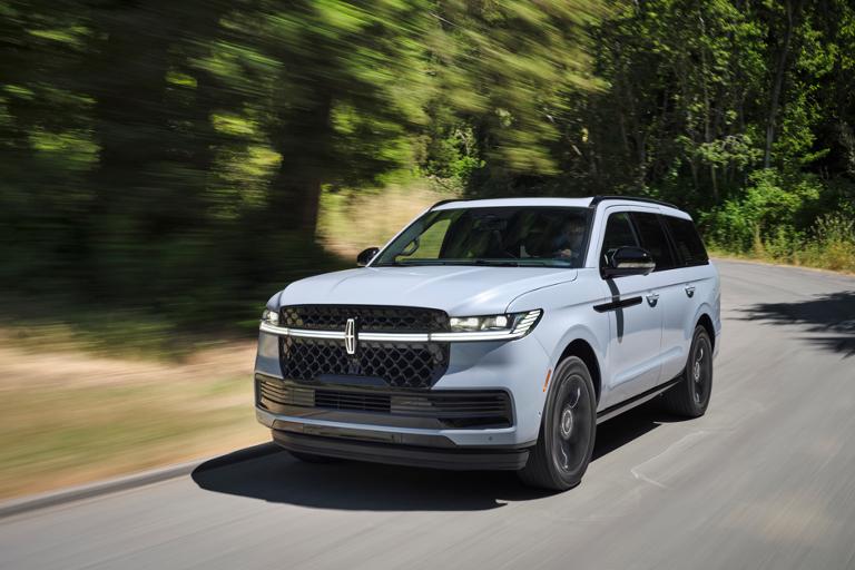 Una Lincoln Navigator® 2026 en gris niebla con el paquete Jet disponible circula por una carretera bordeada de árboles