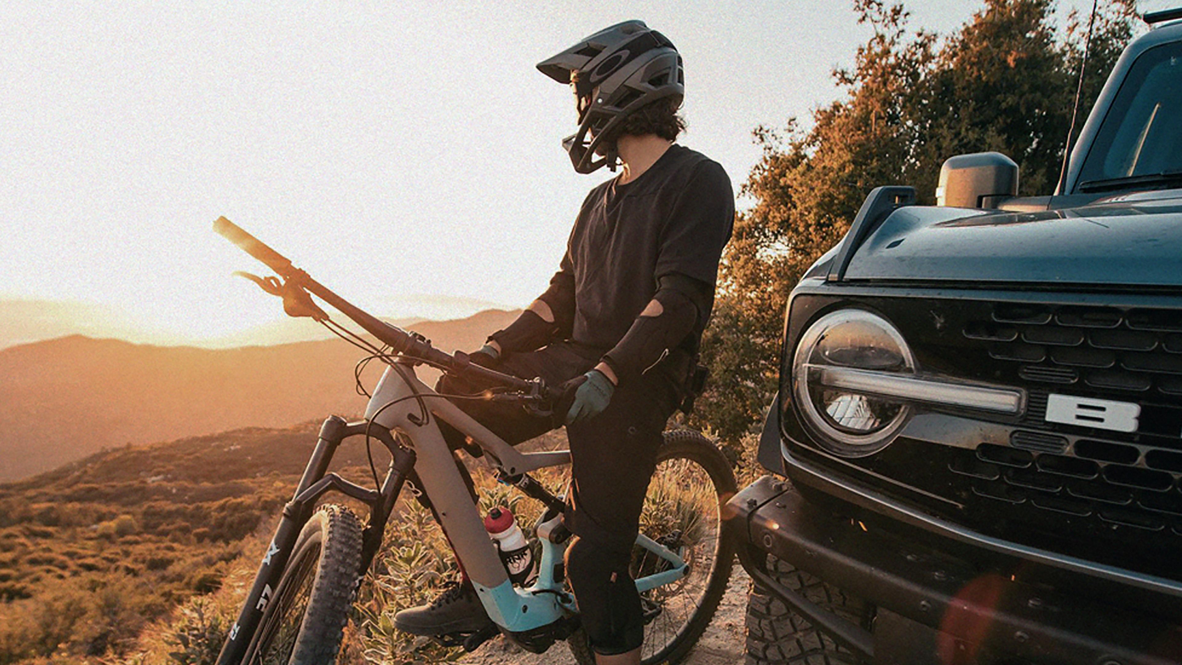 A person sitting astride a dirt bike in protective gear, next to a 2026 Ford Bronco® SUV