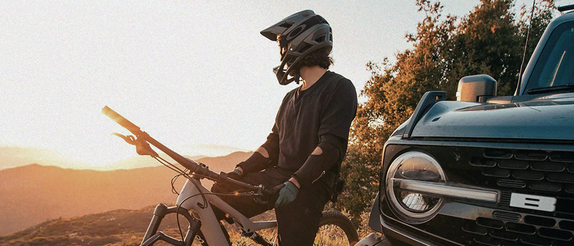 A person sitting astride a dirt bike in protective gear, next to a 2026 Ford Bronco® SUV