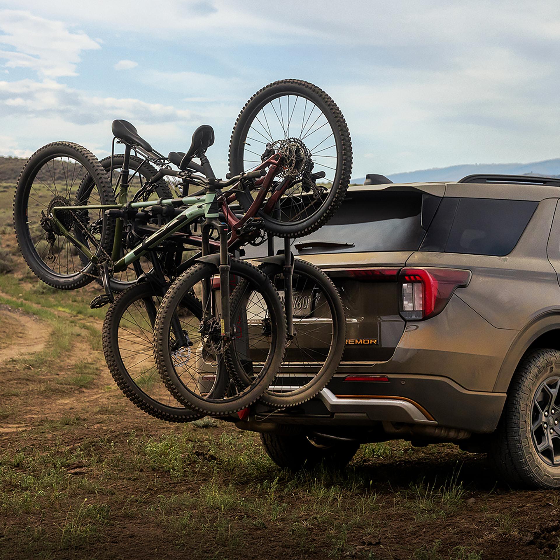 A 2027 Ford Explorer® Tremor® SUV parked on a grassy hillside near a dirt trail, with bikes on an accessory rear rack