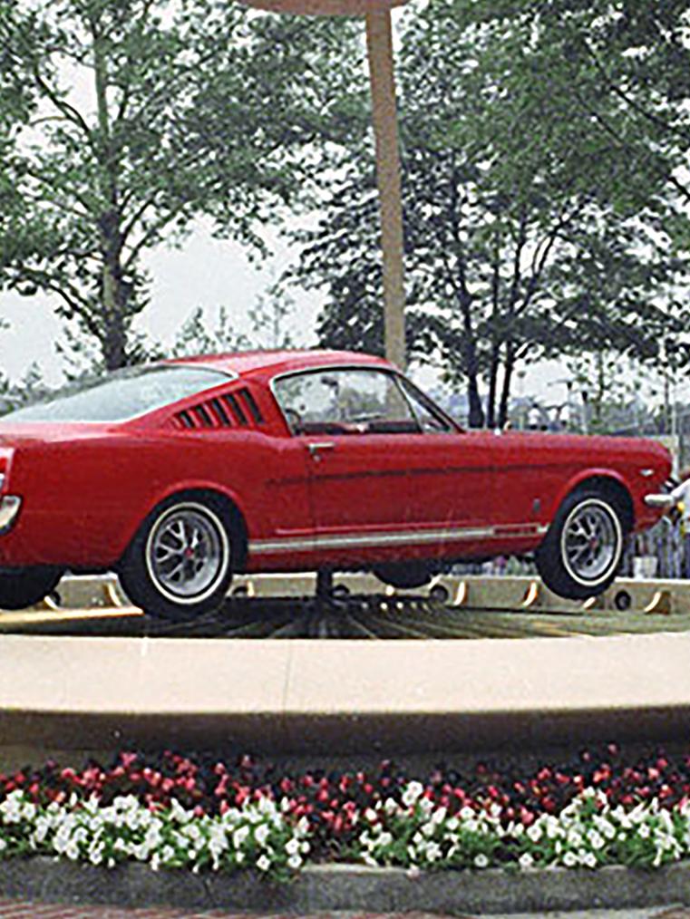 A red 1965 Ford Mustang car on a display platform