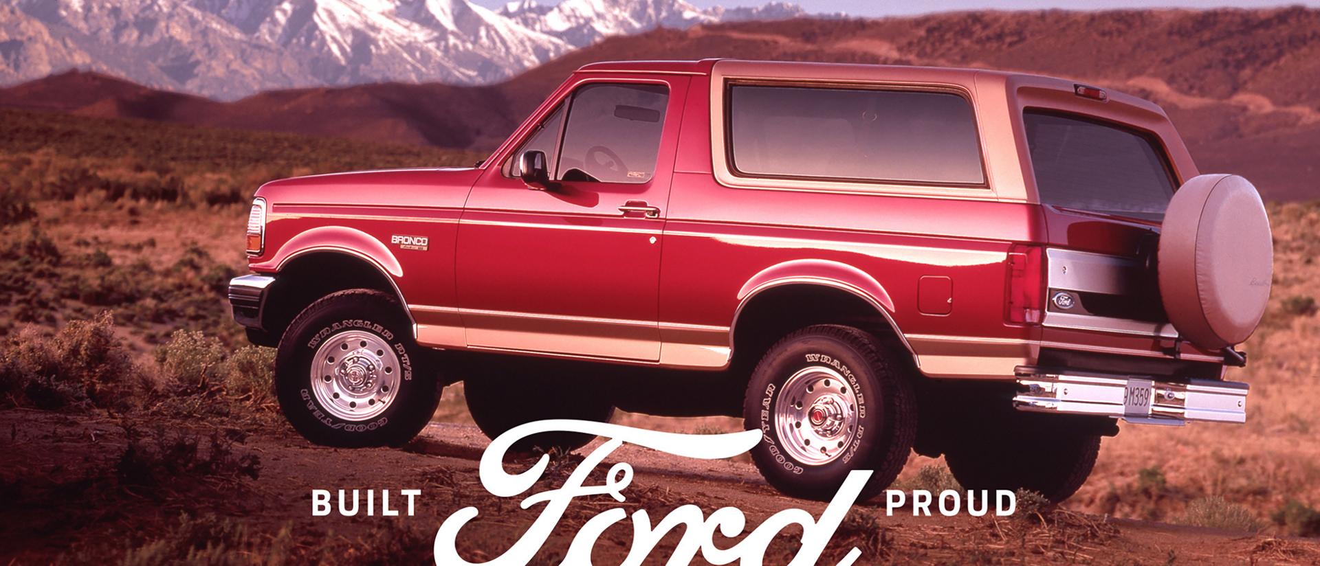 A vintage tri-color Ford Bronco® model parked in front of a mountain landscape