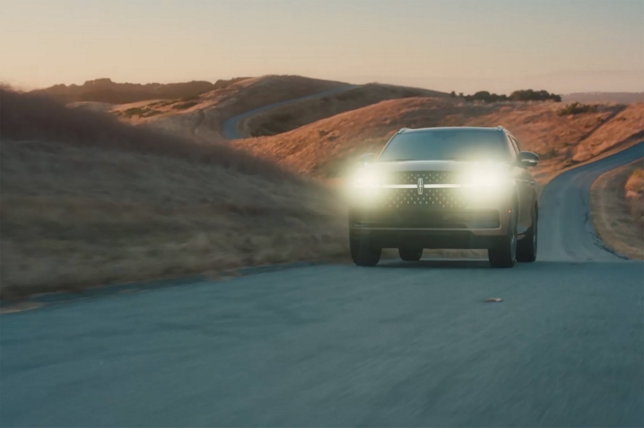 A 2025 Lincoln Navigator® SUV is being driven at dusk with its headlamps illuminated