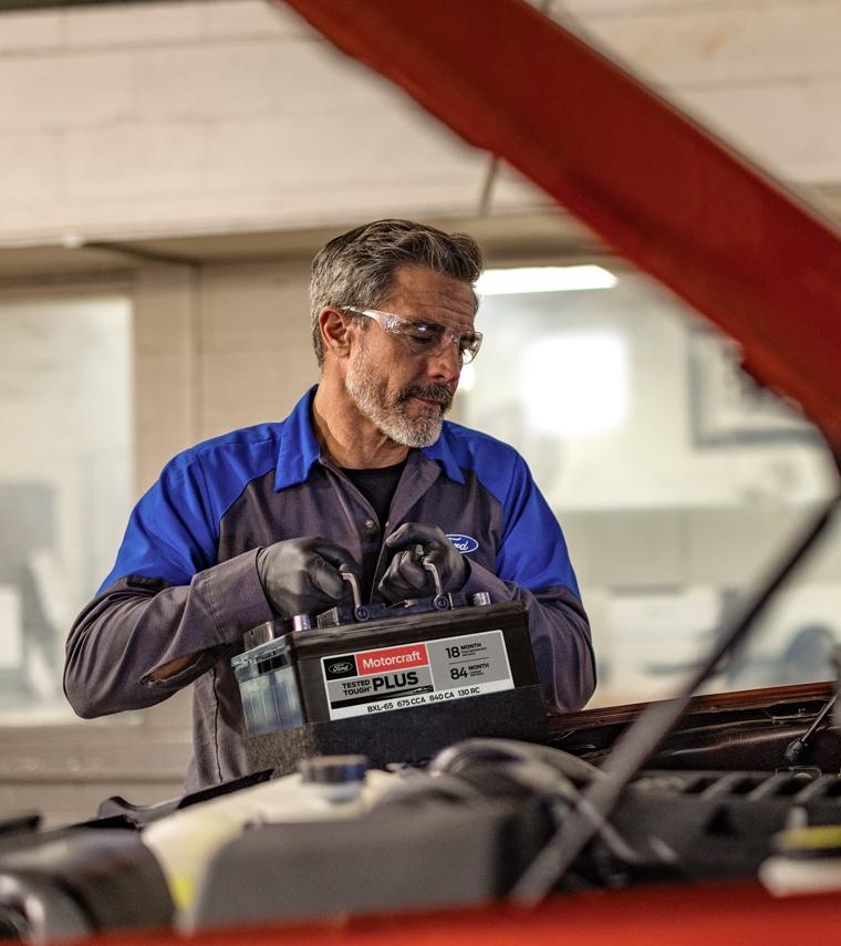 A Ford mechanic holding a battery near a Ford vehicle.  