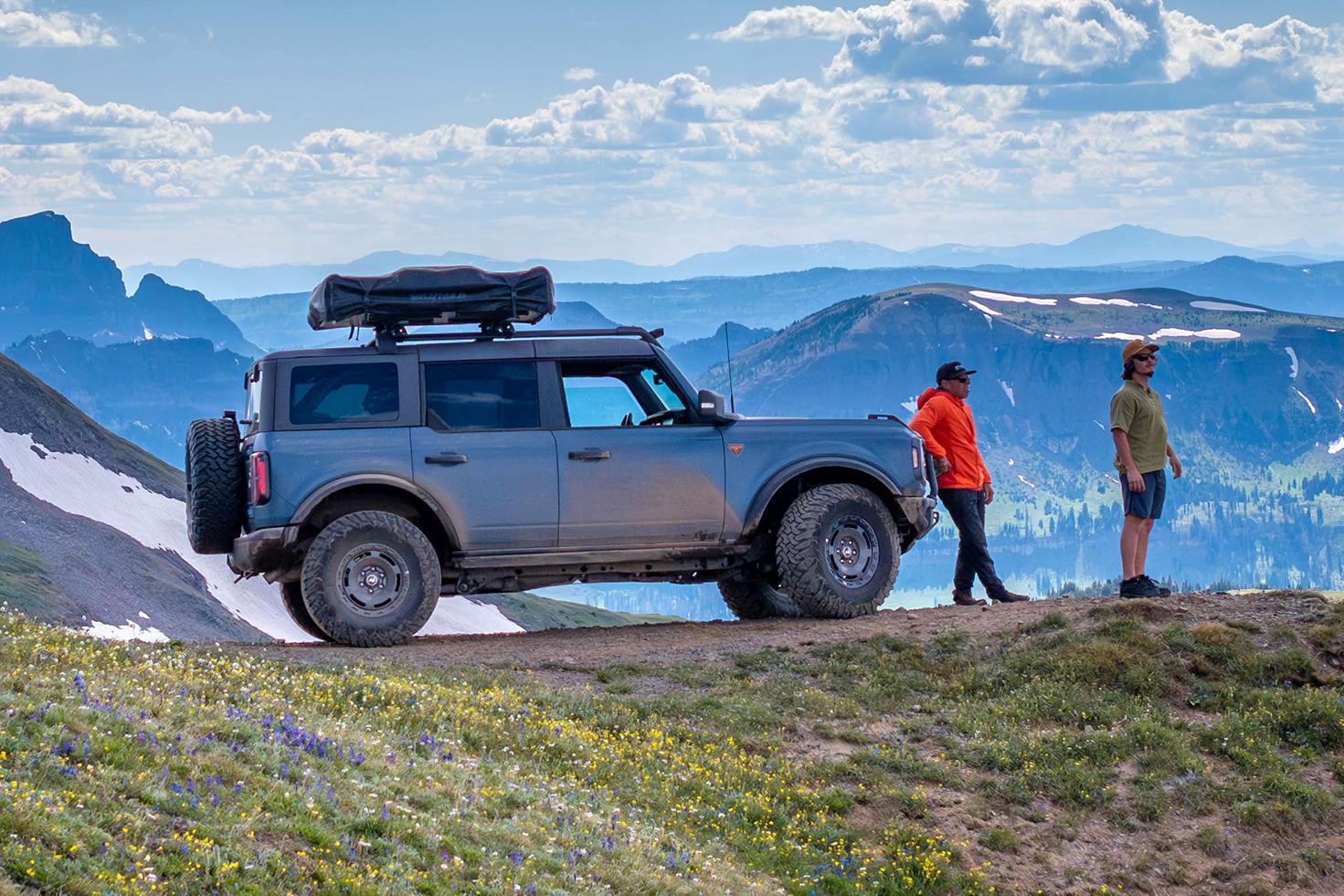 A couple of adults stand outside their Ford Bronco® SUV at an epic mountain overlook to take in the view