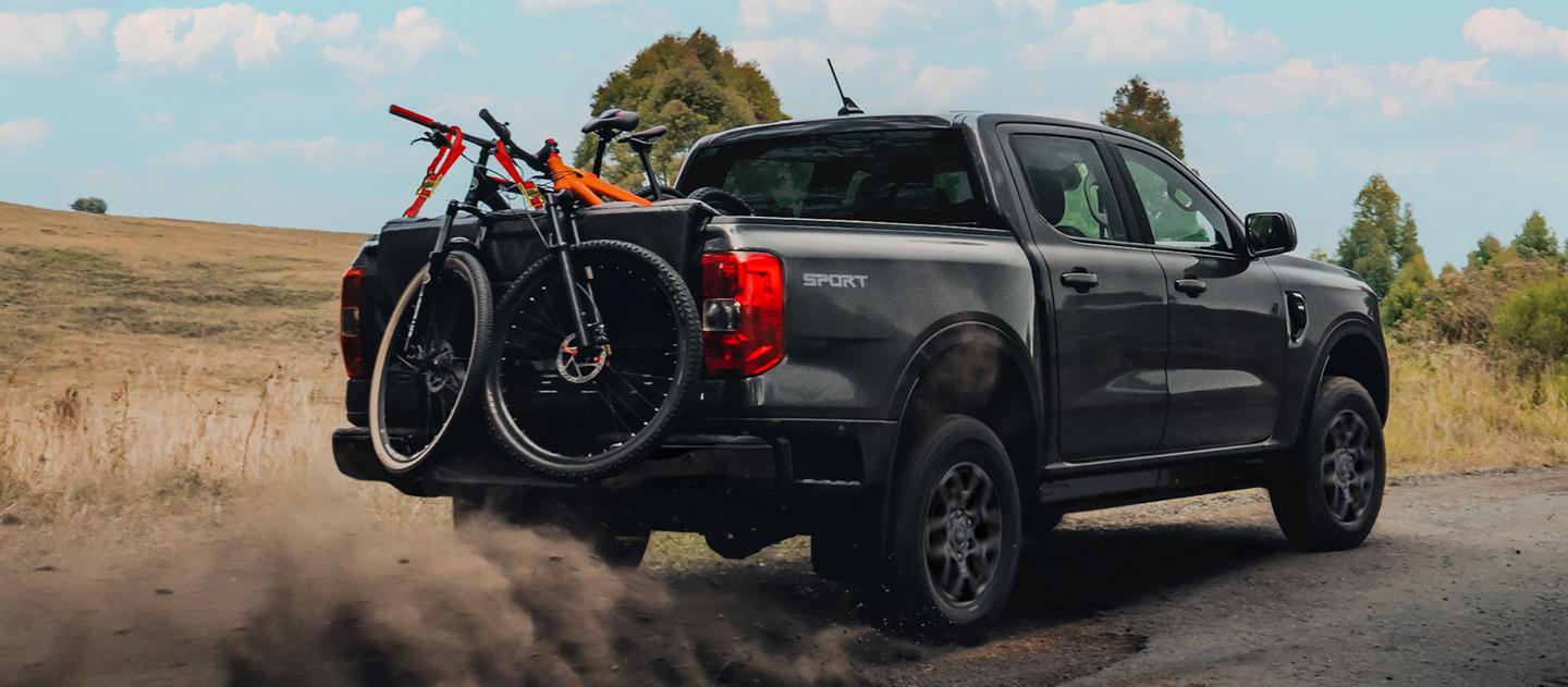 The 2026 Ford Ranger® truck driving on a dirt road with three bicycles in the truck bed