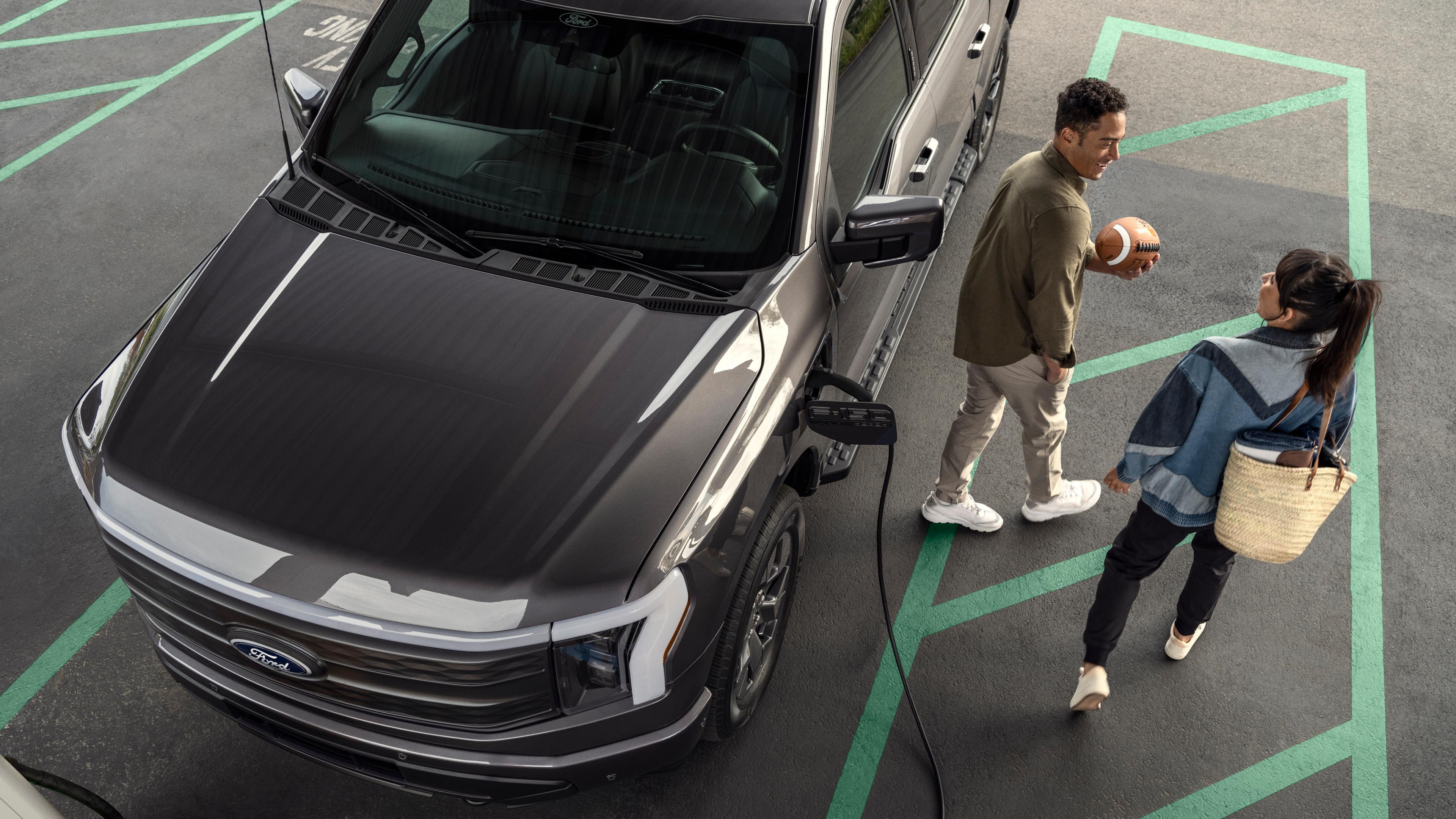 2025 Ford F-150 Lightning plugged into charger in parking lot as couple walk away
