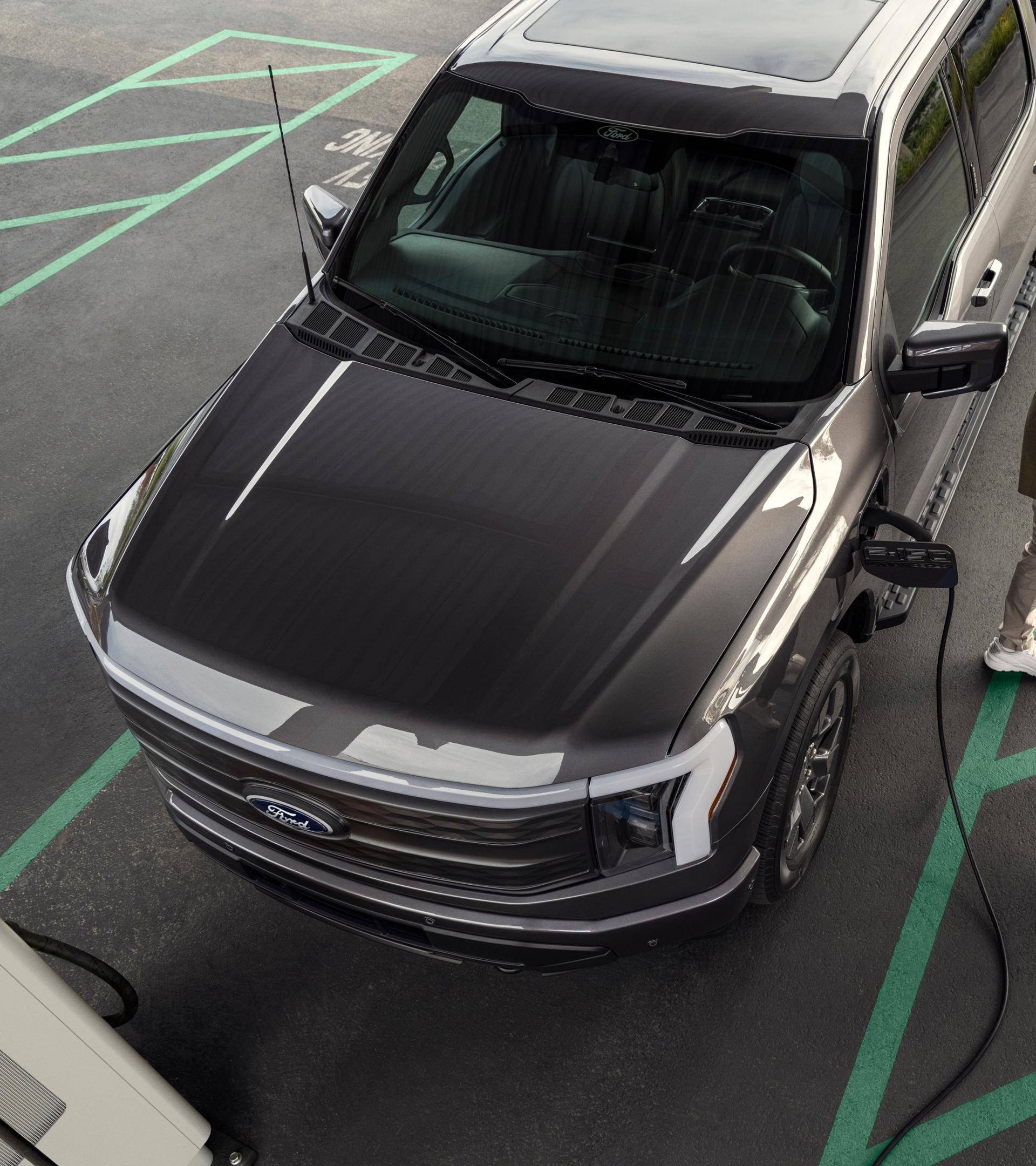 2025 Ford F-150 Lightning plugged into charger in parking lot as couple walk away