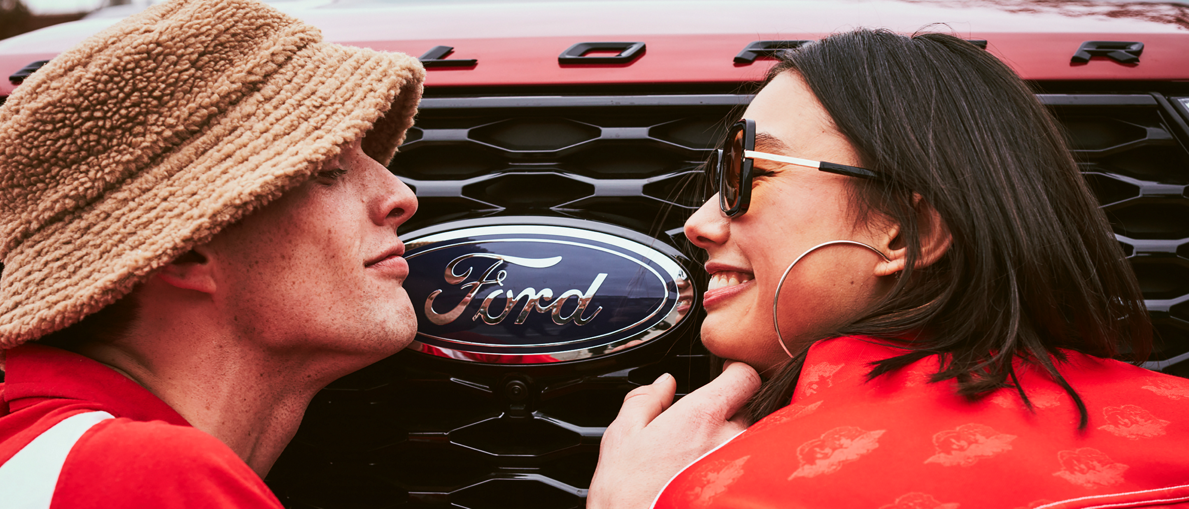 A couple smile at each other in front of a Ford Explorer
