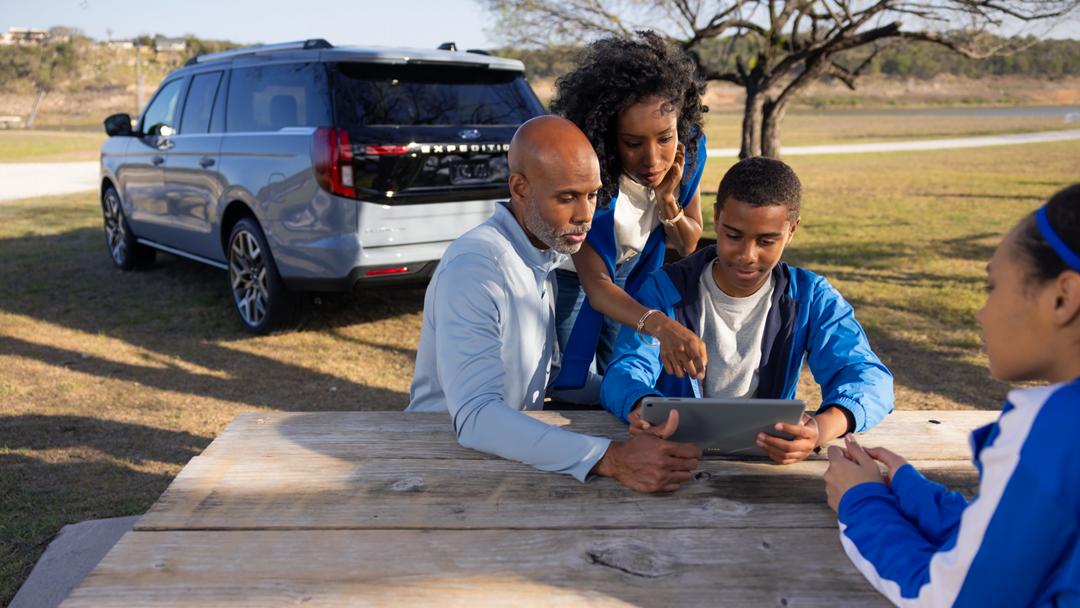 Three people using the Wi-Fi® hotspot with a parked 2027 Ford Expedition® SUV in the background