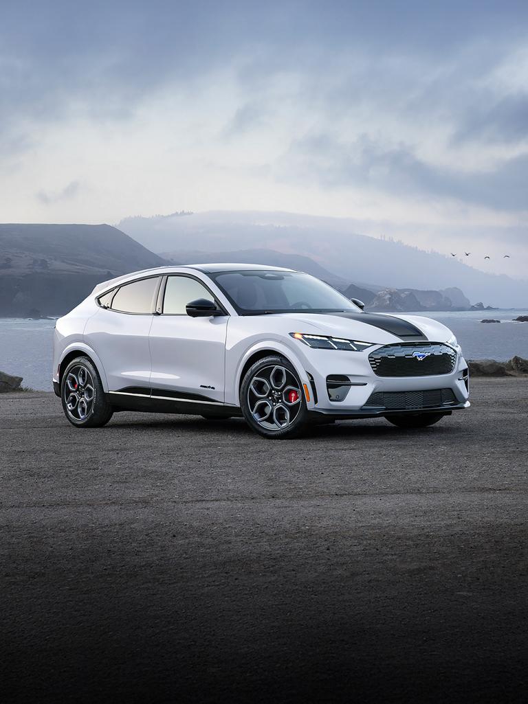 Front end of a 2026 Ford Mustang Mach-E® GT model with hood stripe against a sunset background