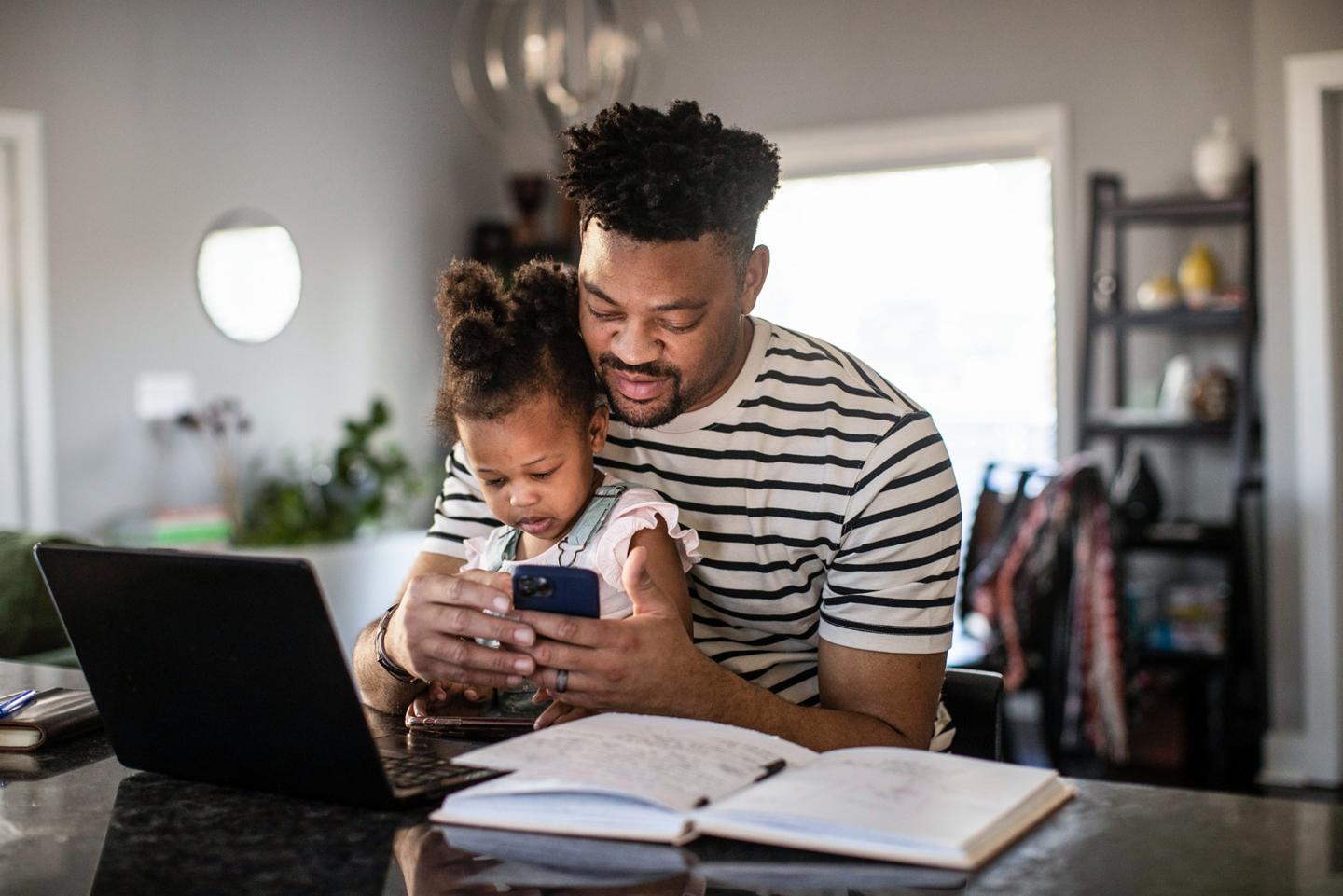 A man holds his child in his lap while interacting with the Ford app on his phone
