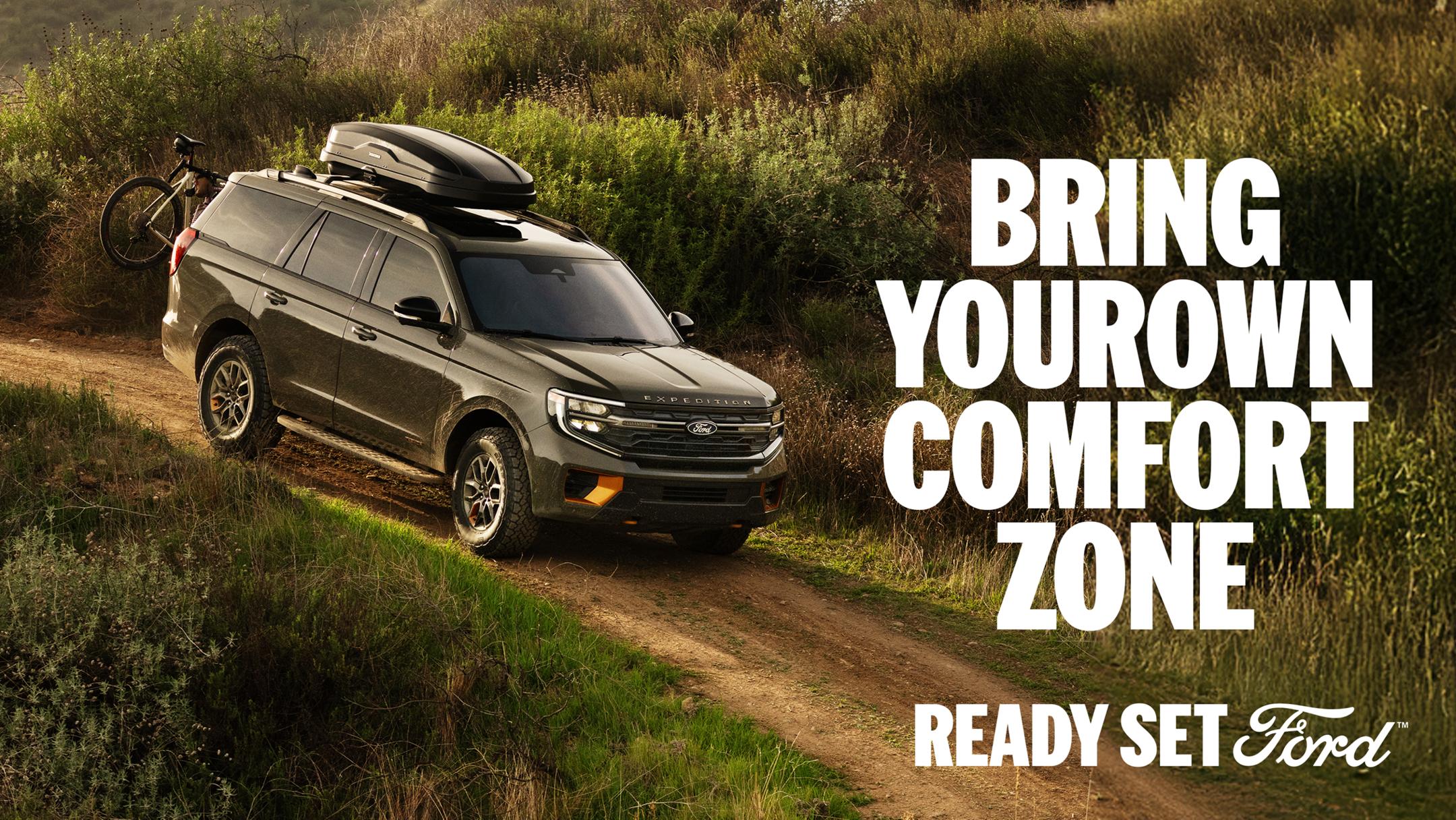 A side profile view of the 2025 Expedition on a dirt trail with a mountain bike mounted on the back. White text “Bring Your Own Comfort Zone” appears in the top-right corner.