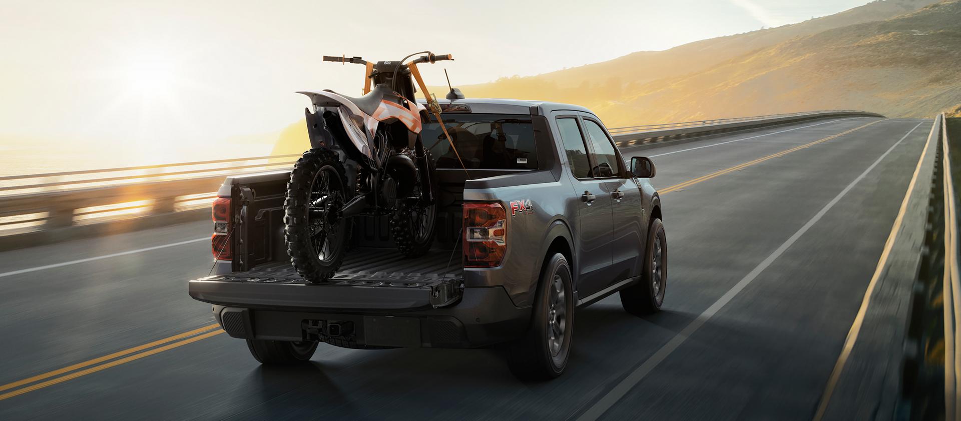 2026 Ford Maverick® Tremor® model with a motorcycle strapped in the bed being driven on the highway
