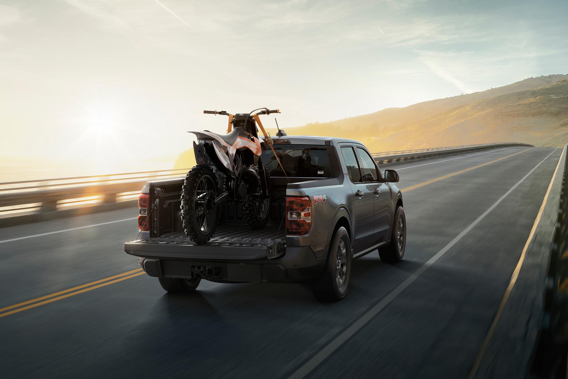 2026 Ford Maverick® Tremor® model with a motorcycle strapped in the bed being driven on the highway