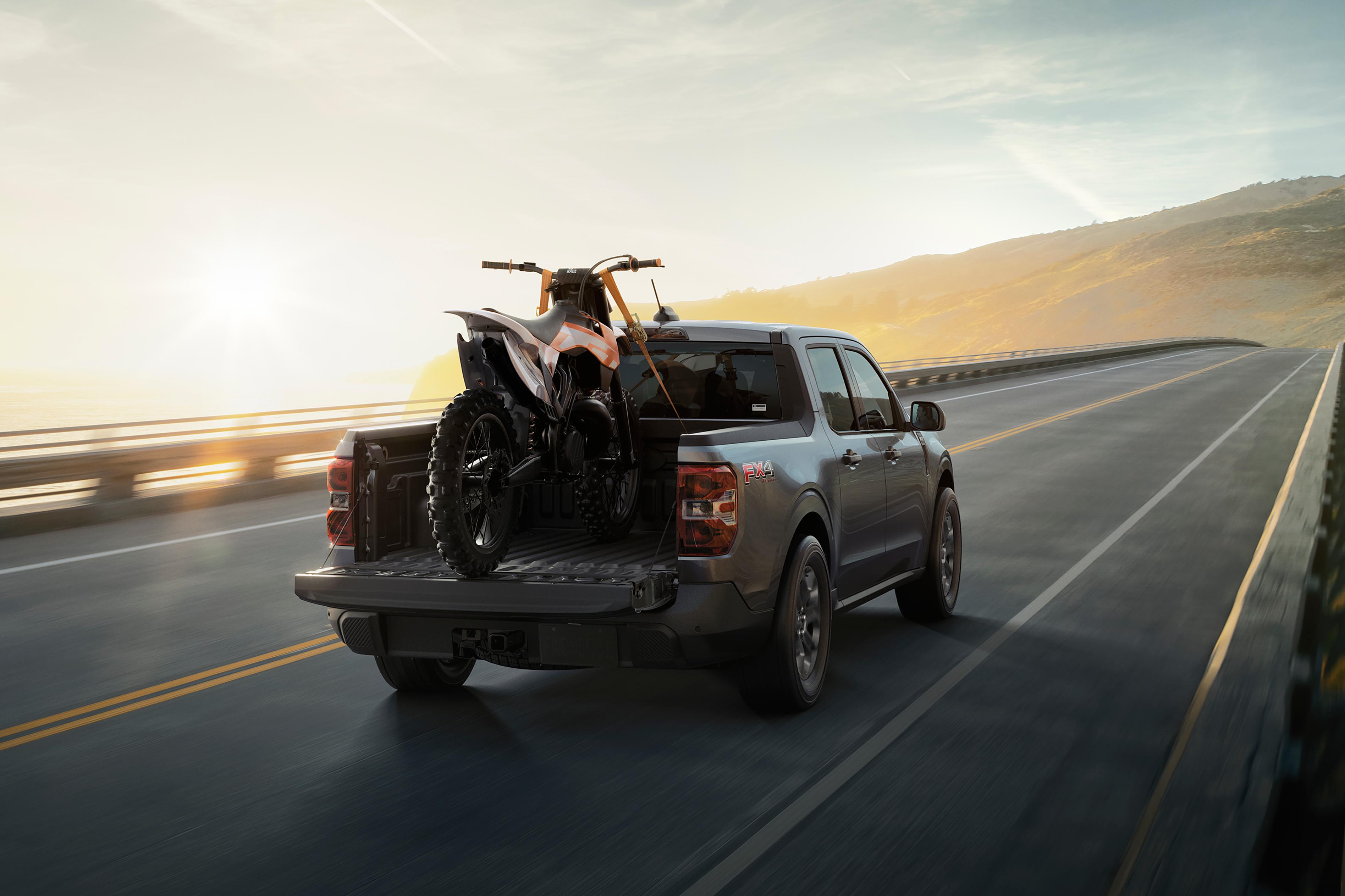 2026 Ford Maverick® Tremor® model with a motorcycle strapped in the bed being driven on the highway