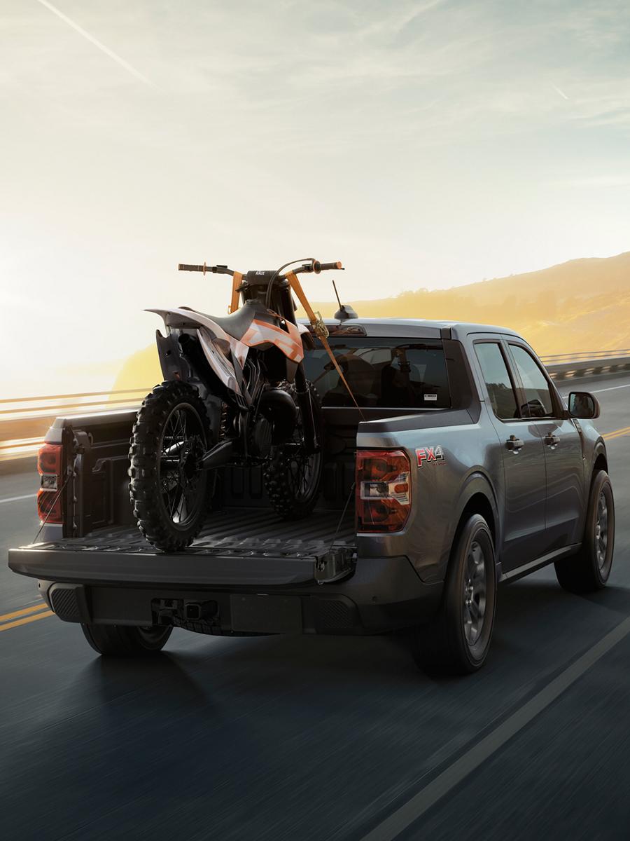 2026 Ford Maverick® Tremor® model with a motorcycle strapped in the bed being driven on the highway
