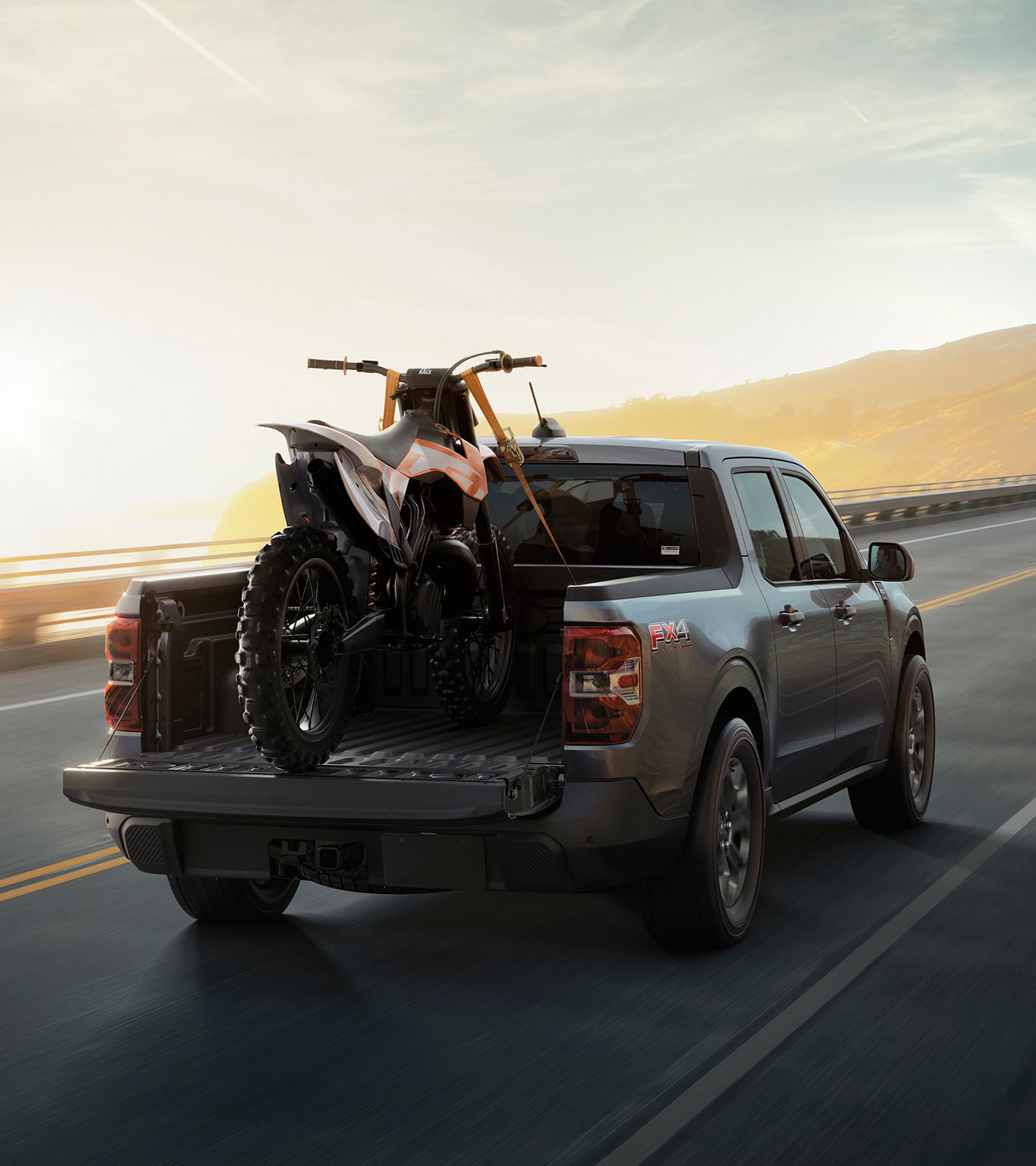 2026 Ford Maverick® Tremor® model with a motorcycle strapped in the bed being driven on the highway
