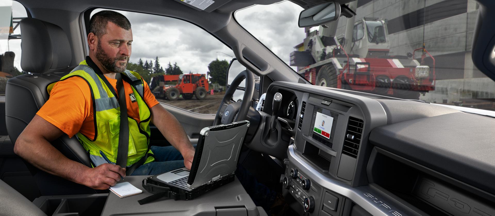 A person inside the cabin of their 2026 Ford Super Duty® truck using a laptop with the interior work surface
