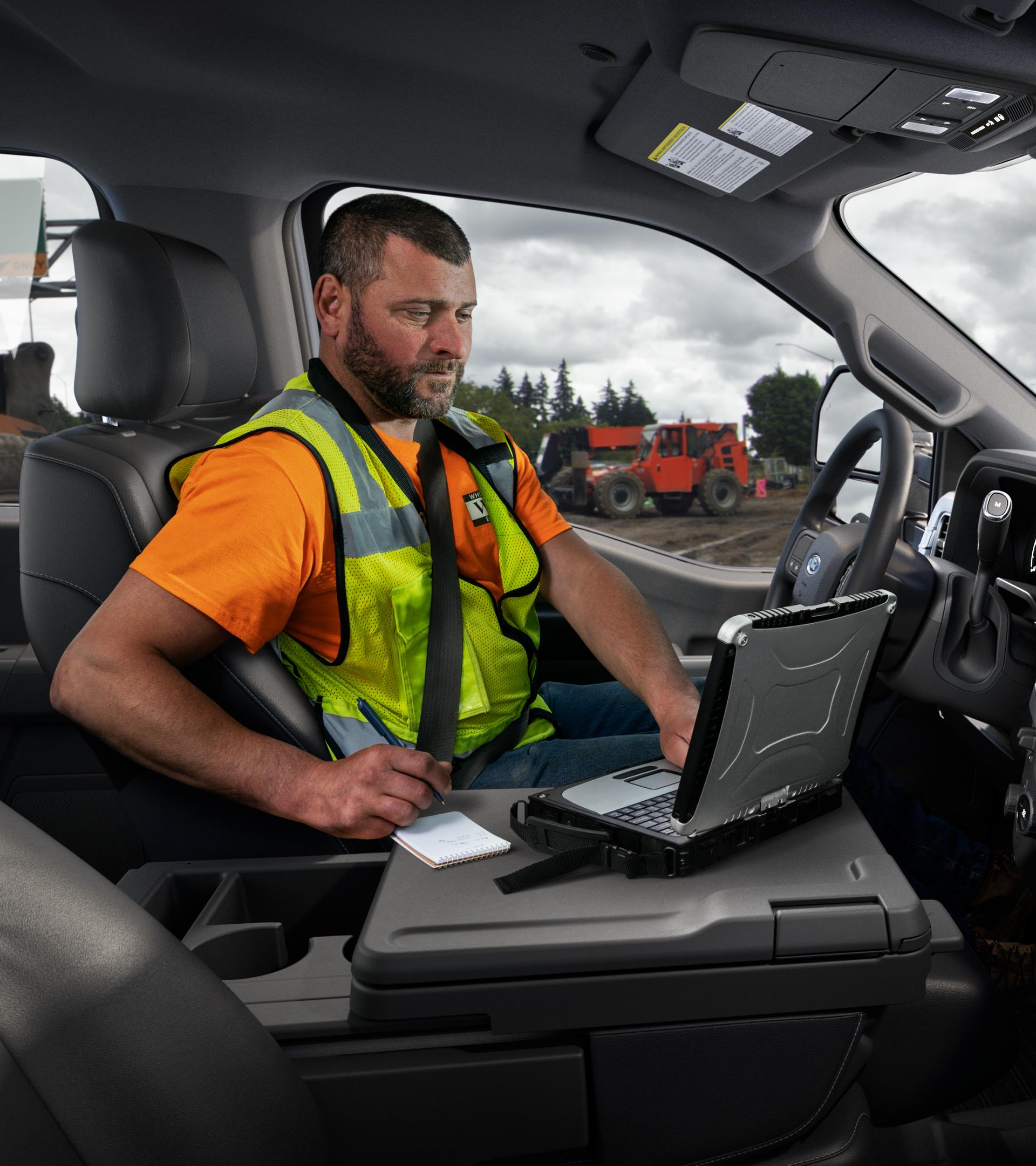 A person inside the cabin of their 2026 Ford Super Duty® truck using a laptop with the interior work surface