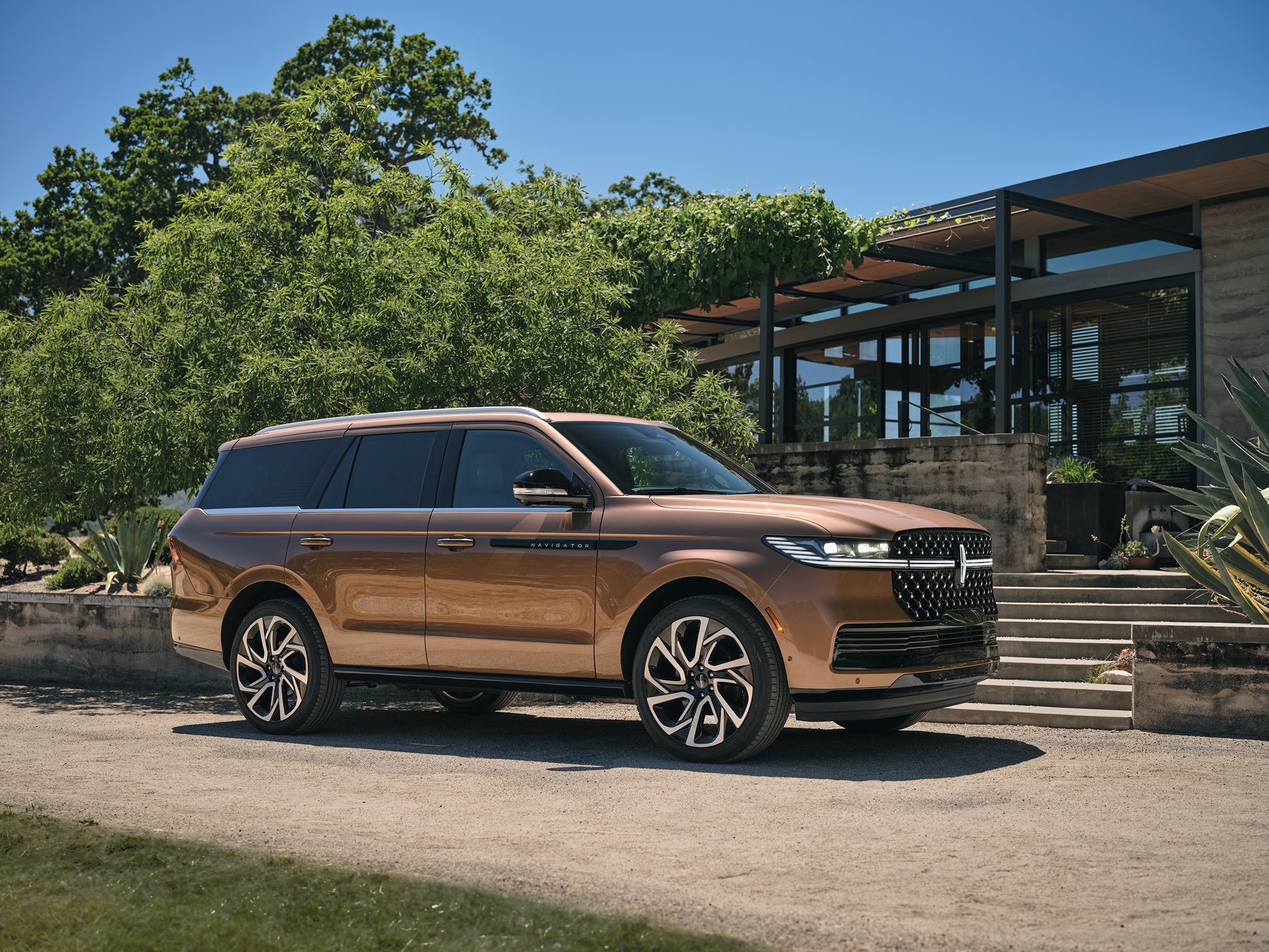 A 2025 Lincoln Black Label Navigator® SUV is parked next to a modern home surrounded by lush greenery.