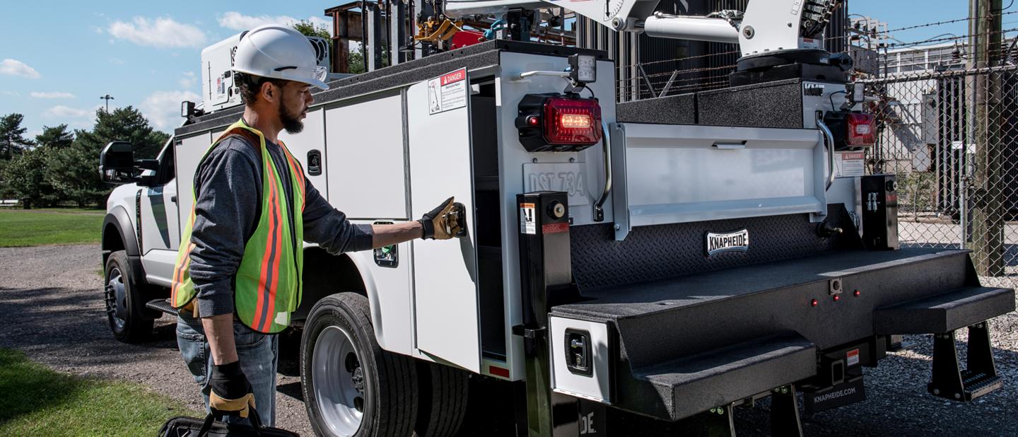 Rear of a 2025 Ford Super Duty® as a worker is opening a door on a utility box