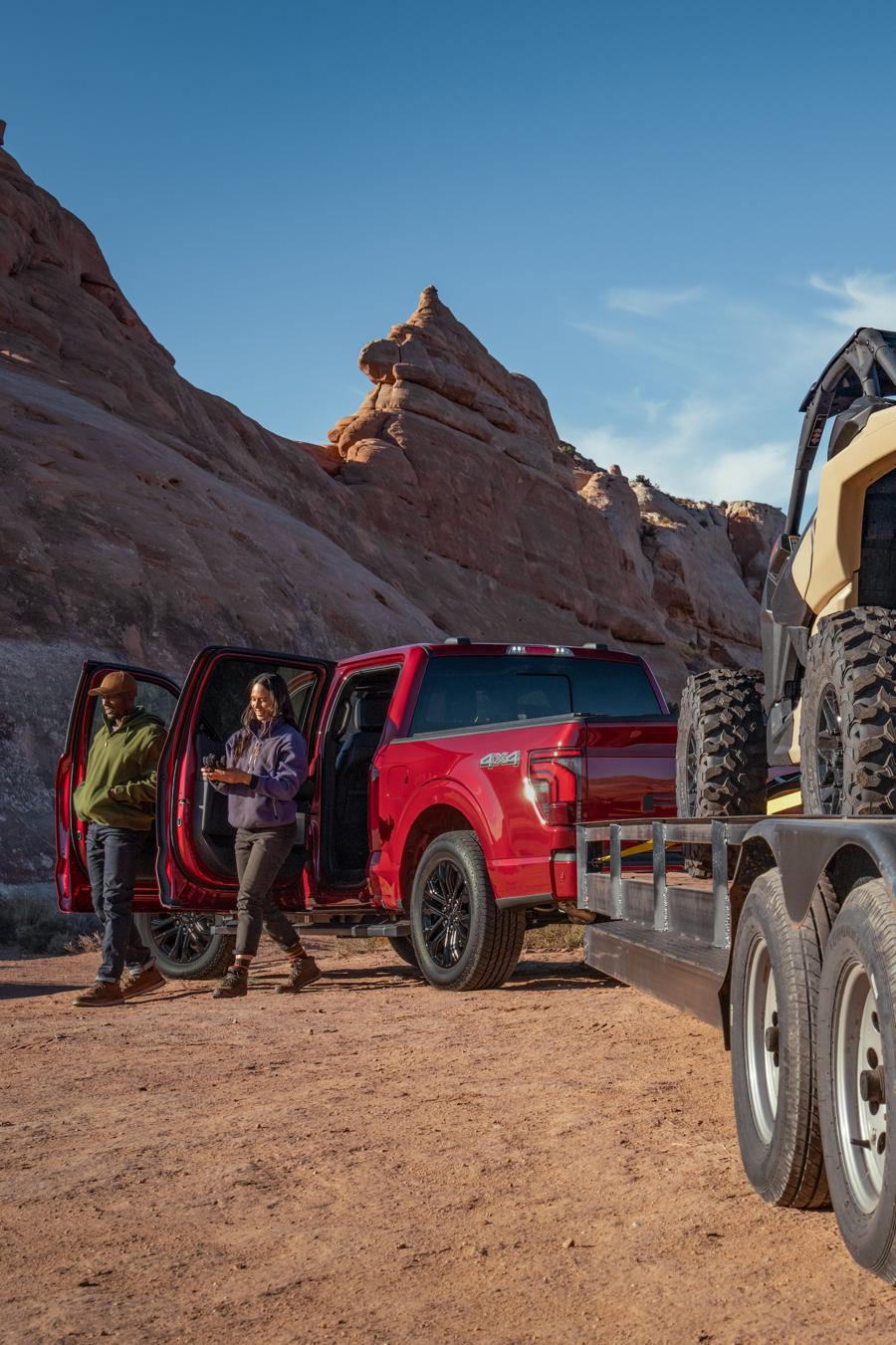Two people walking out of a parked Ford F-150® truck that’s towing multiple ATVs