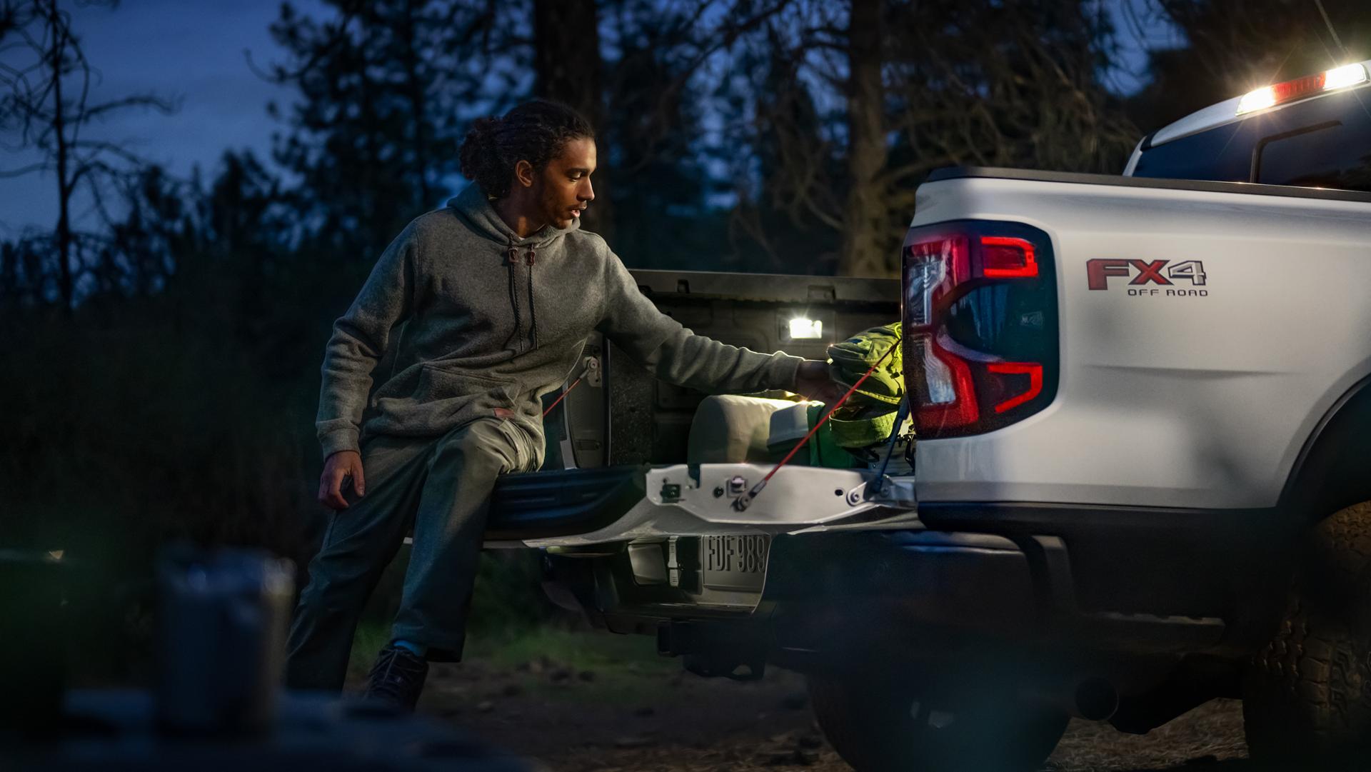 A person loading gear into the bed of their 2026 Ford Ranger® XLT model while sitting on the open tailgate