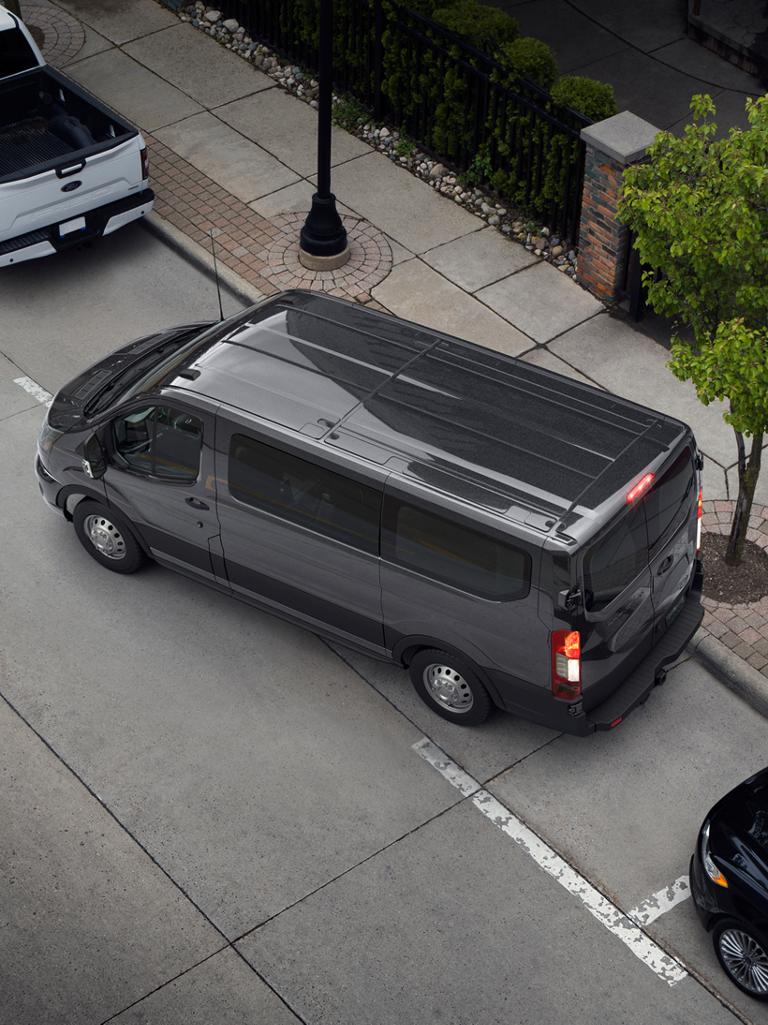 Overhead view of a dark gray 2027 Ford Transit® van parallel parked on a city street between other vehicles
