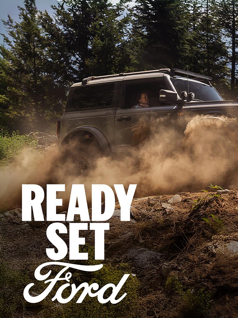 A 2026 Ford Bronco® SUV being driven on a muddy forest trail, with the legend “Ready Set Ford” superimposed