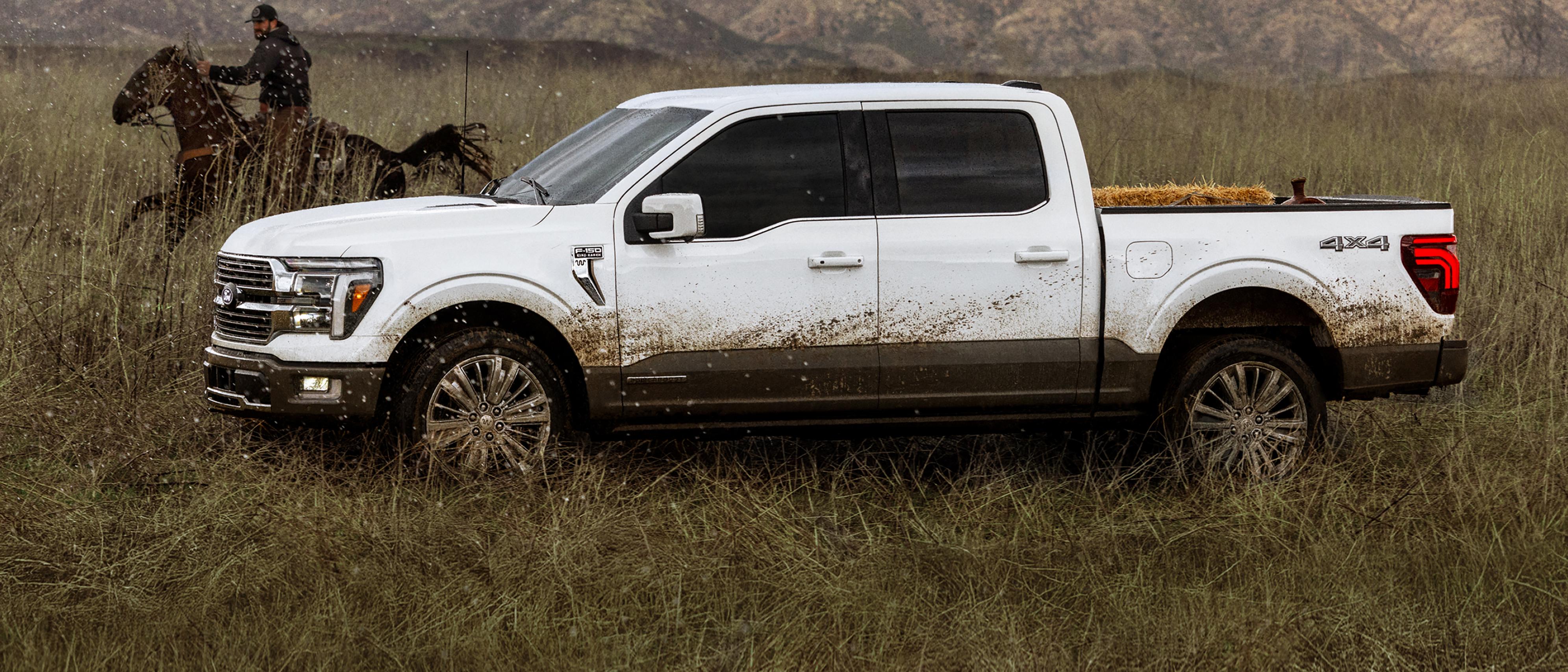 A person riding a horse near a mud splattered 2026 Ford F-150® King Ranch® parked in a field