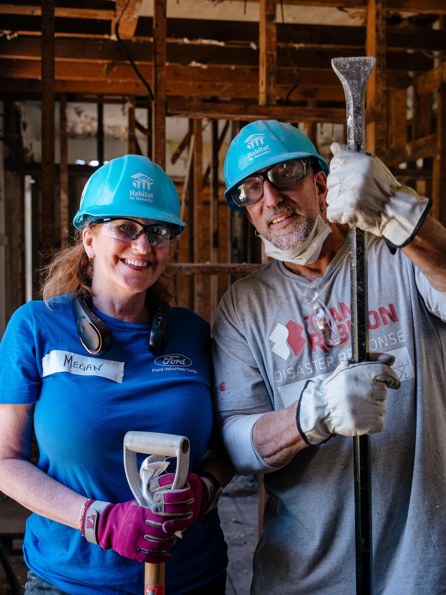 Two people wearing hard hats standing in the structure of a framed out house