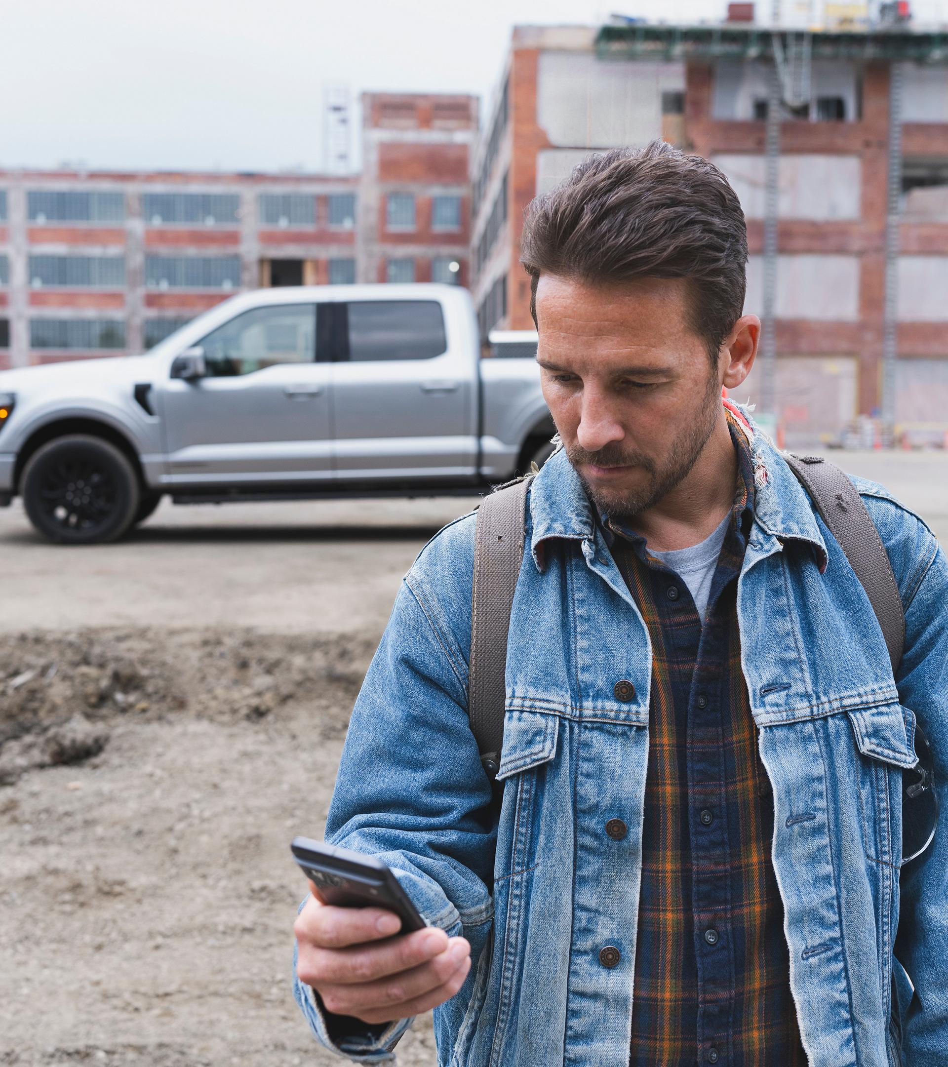 Man looking at his smartphone with a 2027 Ford F-150® pickup in the background parked at a construction site