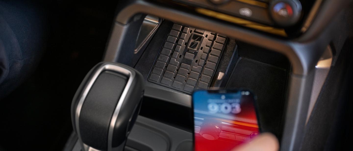 A person's hand placing their phone on the wireless charging pad inside their 2026 Ford Ranger® truck