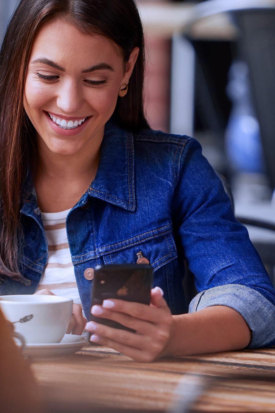 A person sitting at a coffee shop while holding and looking at their cell phone