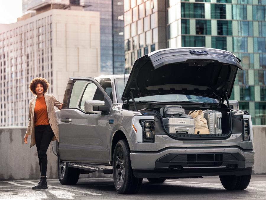 Woman exiting passenger side of an F-150 Lightning® with its frunk open and full of items