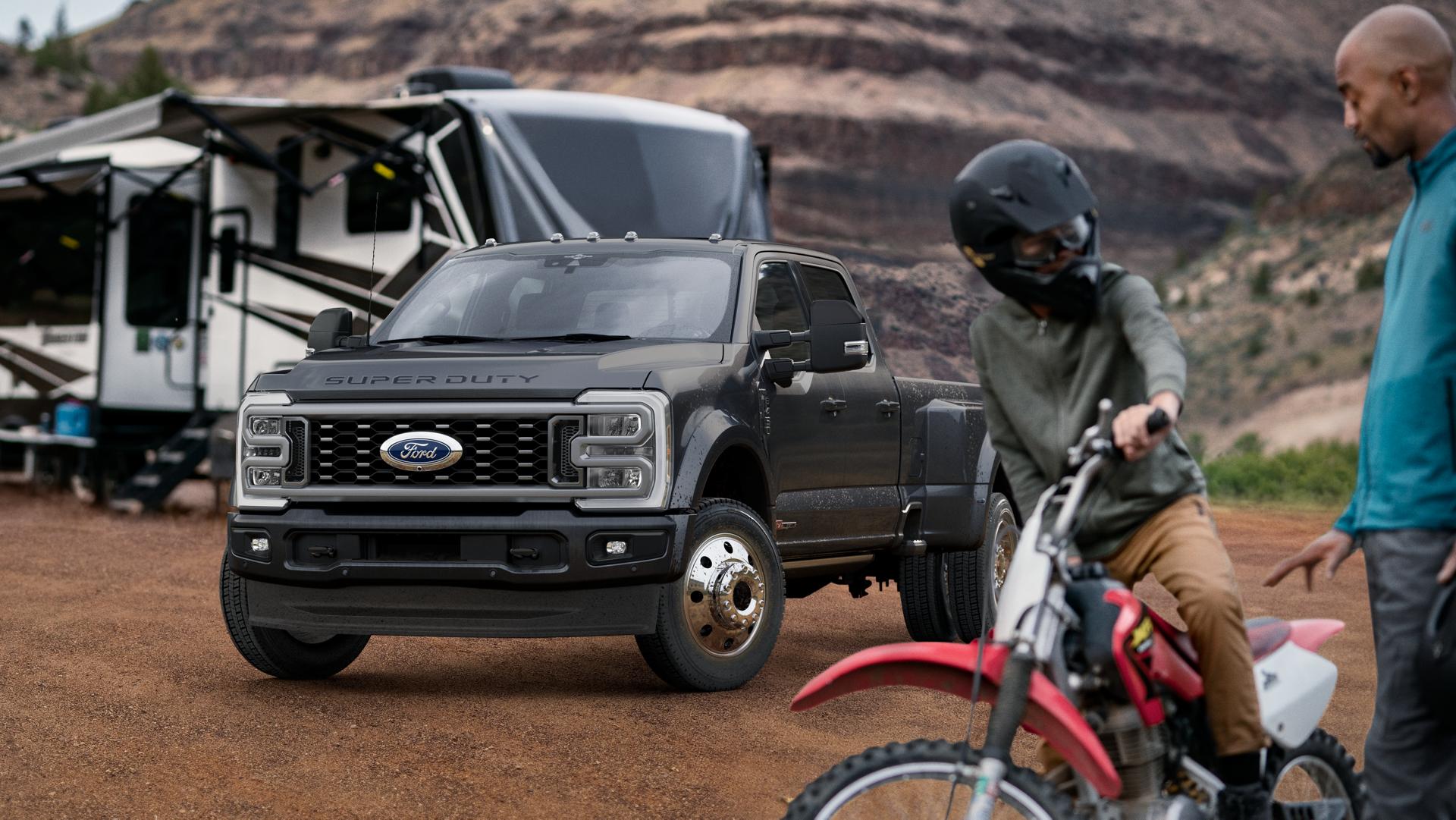 2026 Ford Super Duty® F-450® Platinum® model in Carbonized Gray parked on a campground with a camper in the background