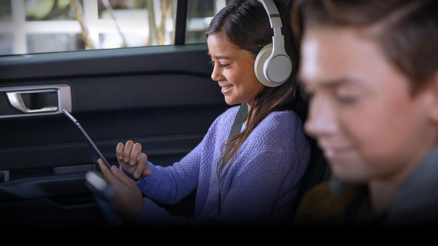 Deux enfants souriants utilisant des appareils mobiles assis dans la deuxième et la troisième rangée d’un VUS Ford.