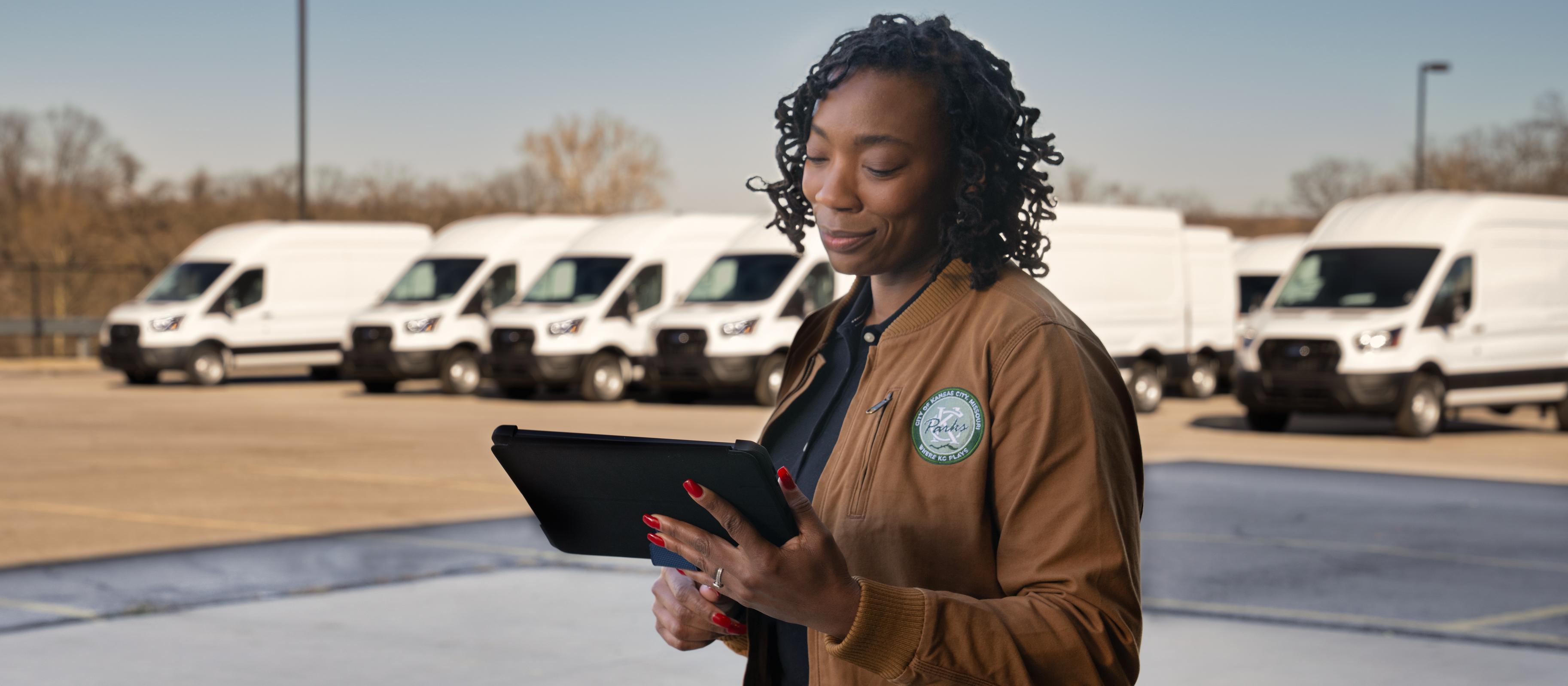 Un parc automobile de véhicules Ford E-Transit™ 2025 blancs stationnés derrière un travailleur tenant une tablette